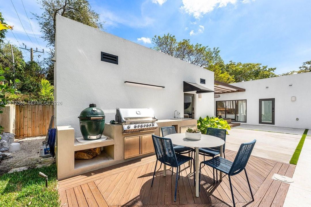 Outdoor kitchen featuring custom concrete cabinetry, stainless steel grill, integrated sink, and wood-finish decking