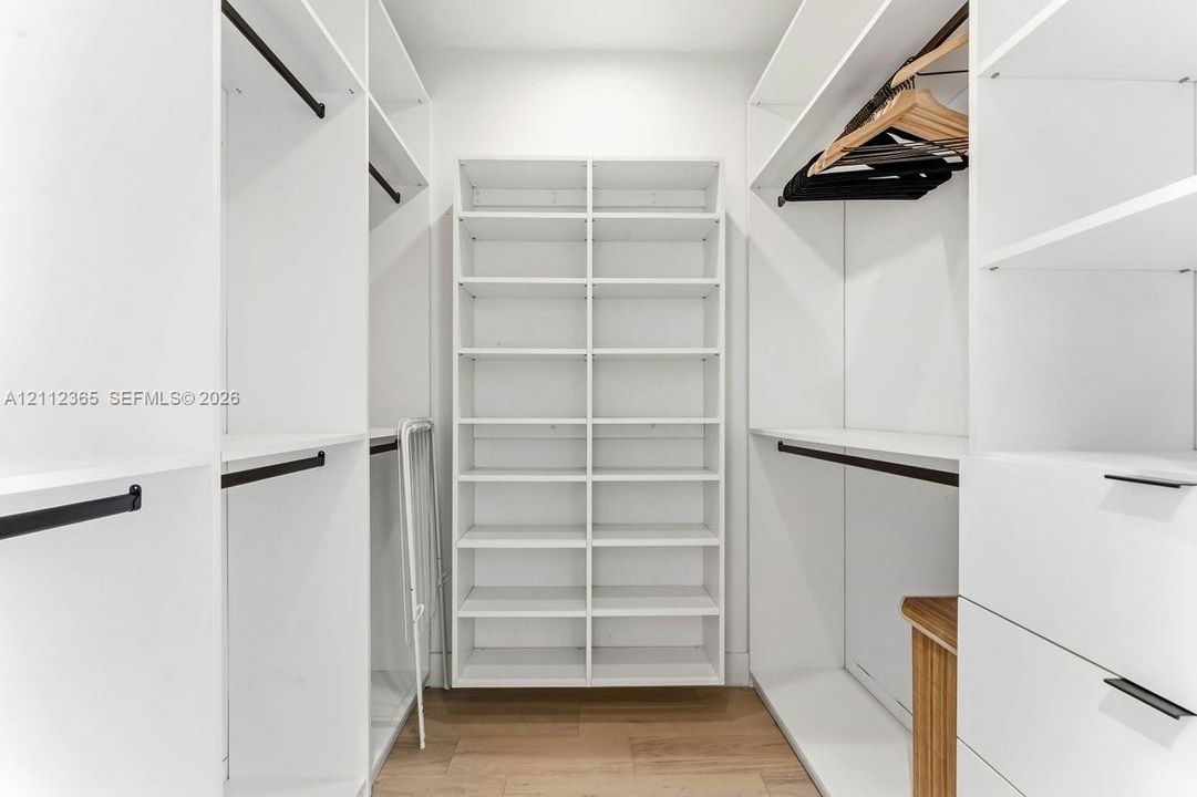 Custom walk-in closet featuring white built-in shelving, multiple hanging rods, integrated drawer storage, and wood-finish flooring