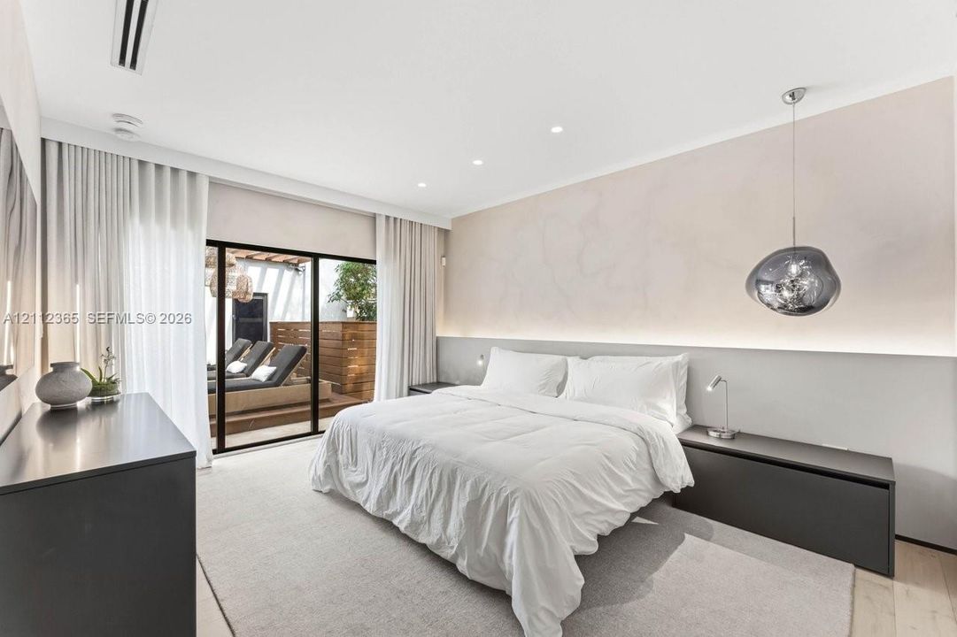Floor-to-ceiling sliding glass doors, built-in recessed lighting, integrated wall-mounted headboard with accent lighting, and sculptural glass pendant fixture