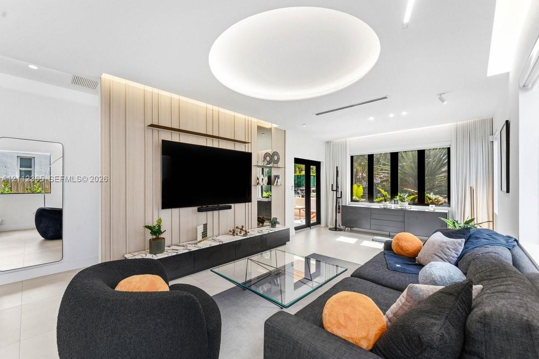 Living area featuring a custom vertical-slat accent wall with integrated shelving, recessed circular ceiling lighting, large-format tile flooring, and a low-profile media console with stone-finish countertop