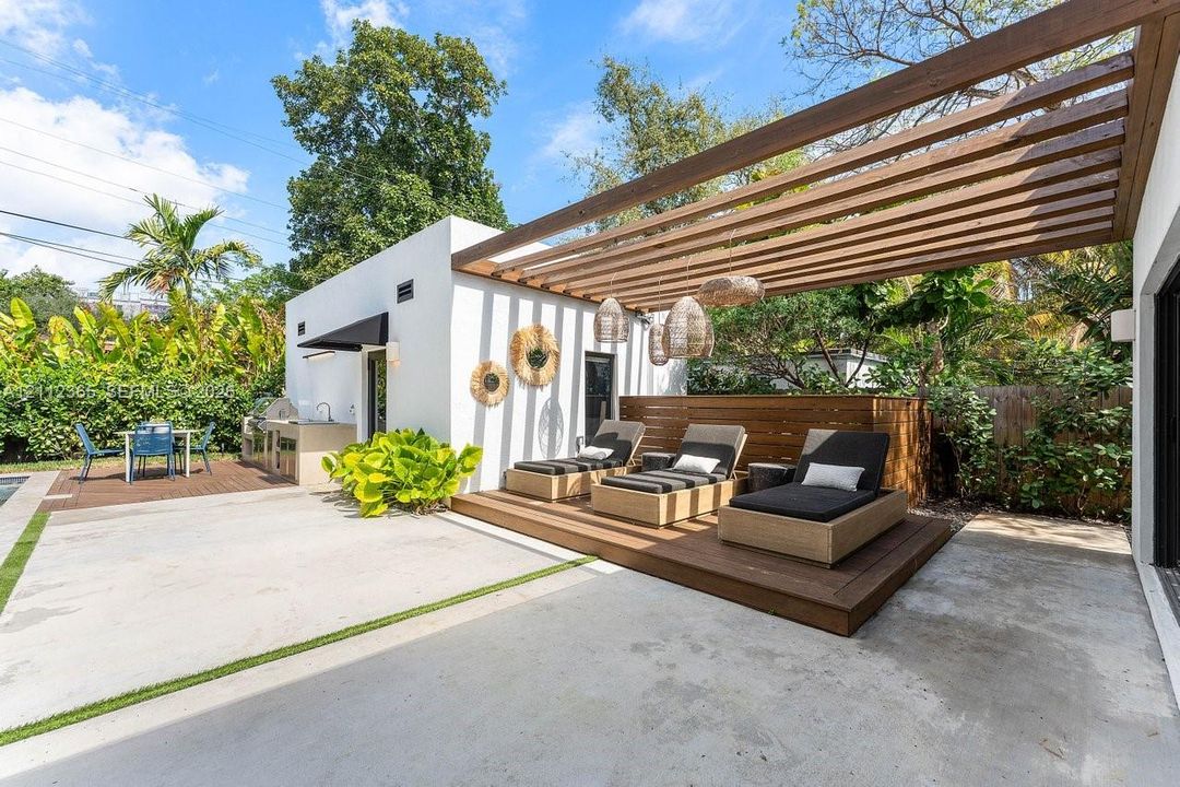 Outdoor patio featuring a built-in outdoor kitchen with sink, a raised wood-finish deck, and a wood-slat pergola