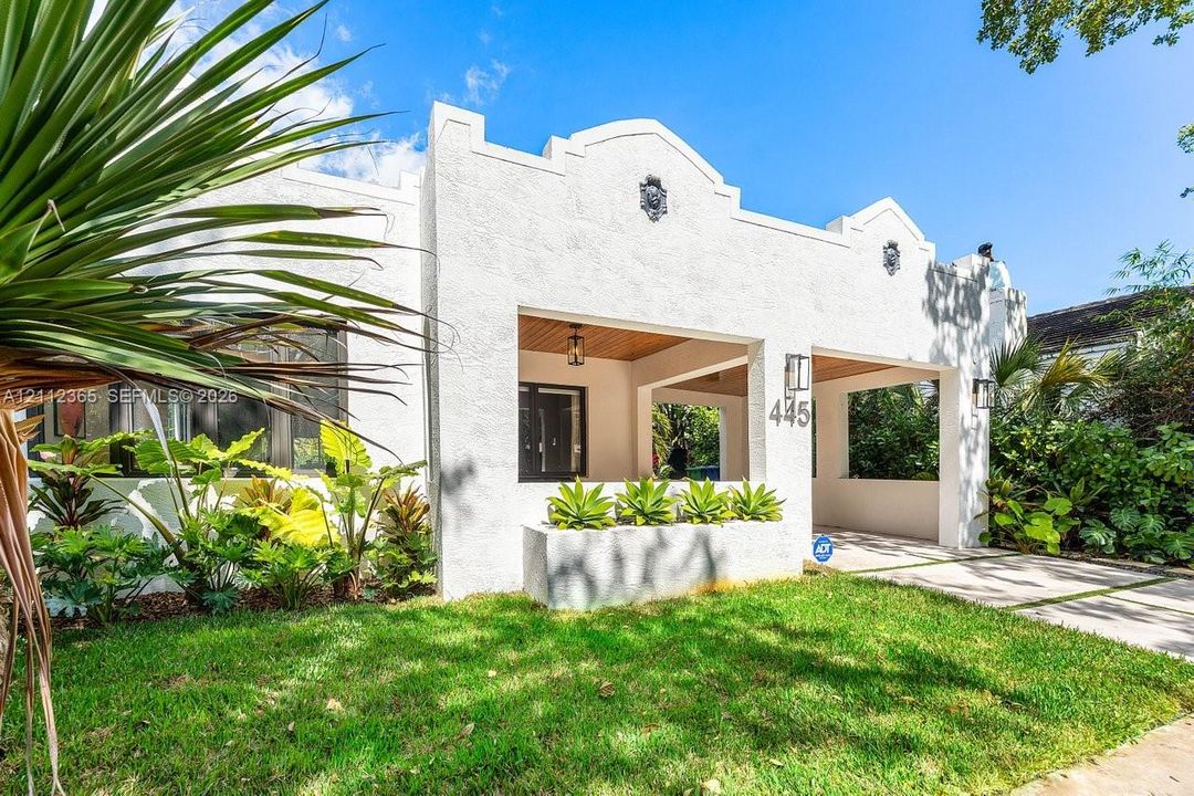 Spanish Revival exterior featuring a textured white stucco facade, parapet roofline with decorative medallions, covered front porch with wood-plank ceiling, and integrated concrete planter boxes