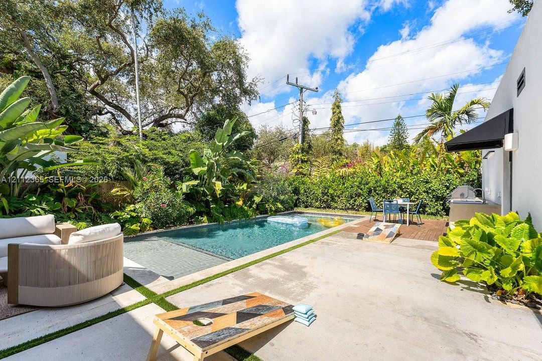Backyard featuring a concrete patio, rectangular swimming pool, wood-plank decking, and mature tropical landscaping