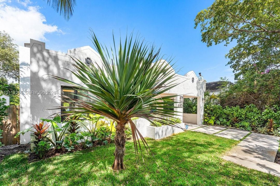 Stucco exterior featuring a Mission-style parapet roofline, covered entryway, and stone-paver walkway with grass inlays