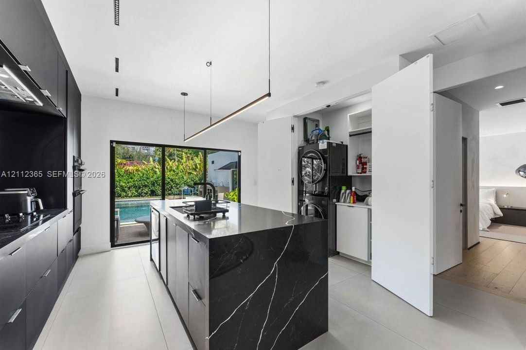 Kitchen featuring black cabinetry, center island with a stone-finish waterfall countertop, matte black fixtures, recessed linear lighting, and sliding glass doors