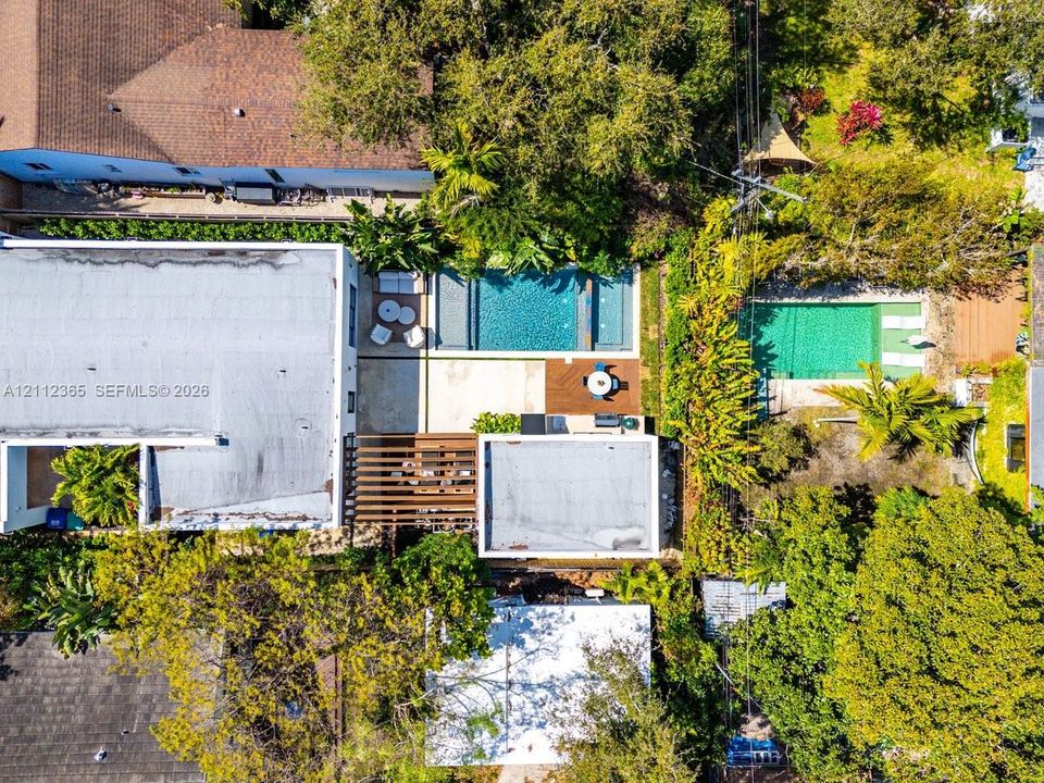 Aerial view of a residential lot featuring an in-ground swimming pool, wood-slatted pergola, paved patio, and mature landscaping