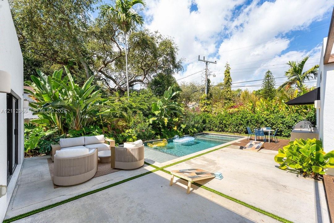 Outdoor patio featuring concrete pavers with synthetic grass inlay, in-ground swimming pool, and built-in outdoor kitchen station