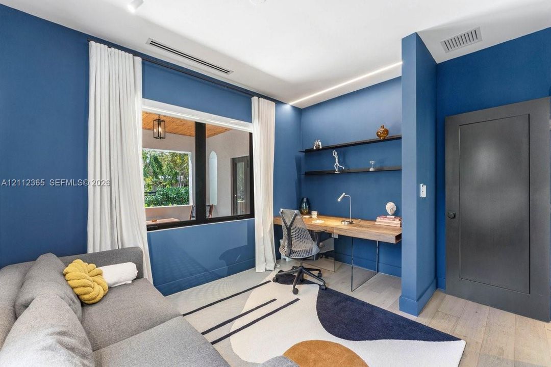 Room featuring wood-finish flooring, recessed ceiling lighting, built-in wall shelving, a wall-mounted desk, and black paneled door