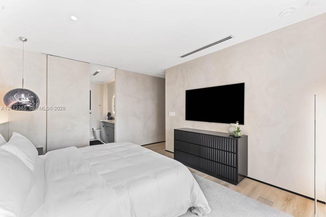 Minimalist interior featuring textured wall finishes, integrated linear air diffusers, wood-finish flooring, and a modern pendant light fixture