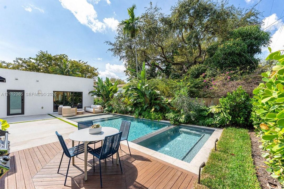 Outdoor space featuring an in-ground pool with integrated spa, concrete patio, wood-finish decking, and established landscape perimeter