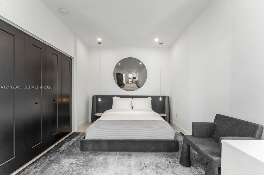 Wall-to-wall black cabinetry with recessed hardware, circular wall mirror, dual pendant light fixtures, and recessed ceiling lighting
