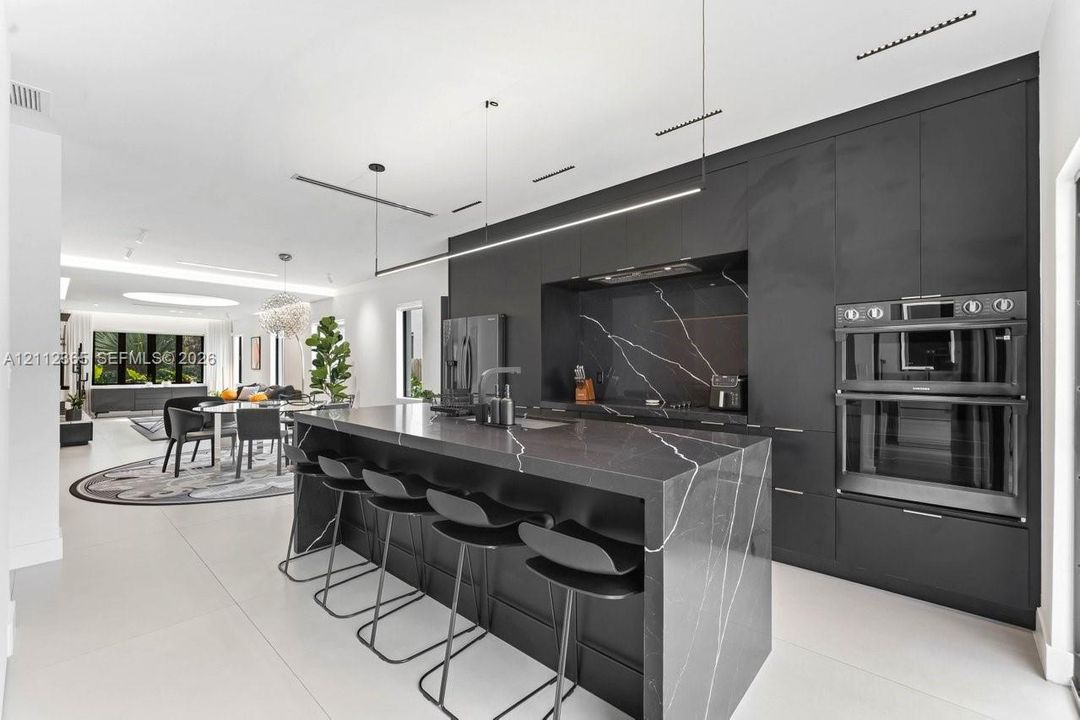 Kitchen featuring matte black floor-to-ceiling cabinetry, dark stone-finish waterfall island with waterfall edge, integrated stainless steel double wall oven, and linear pendant lighting