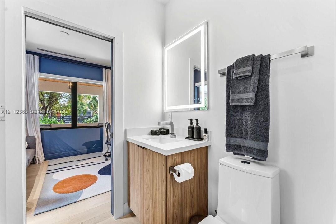 Bathroom featuring a wood-finish vanity with a stone countertop, an integrated rectangular sink, a wall-mounted brushed metal faucet, and an illuminated vanity mirror