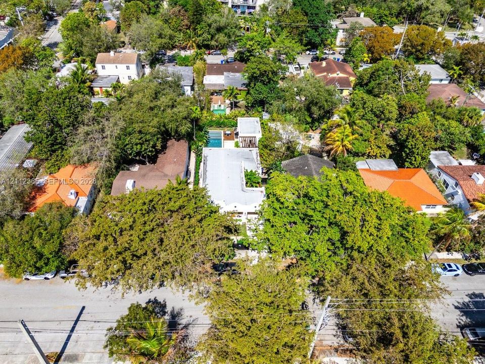 Aerial perspective of a property featuring a swimming pool, a flat roofline, mature trees, and dense foliage within a residential lot