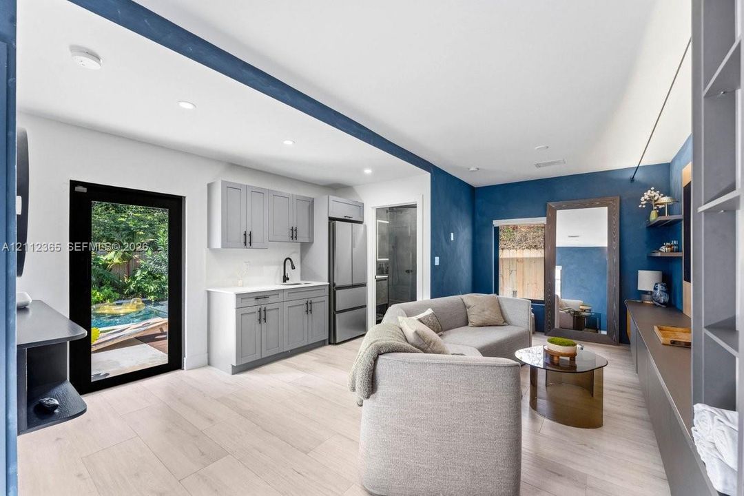 Kitchenette featuring light gray shaker-style cabinetry, quartz countertops, a stainless steel refrigerator, and wood-finish flooring, complemented by recessed lighting and a glass-paneled exterior door
