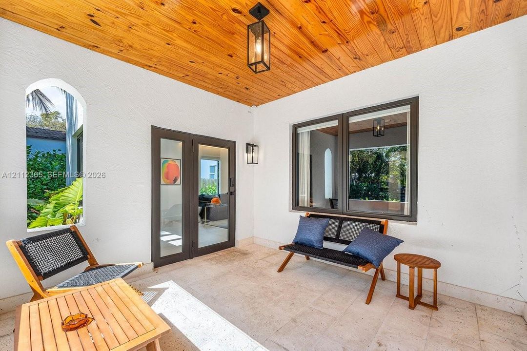 Covered patio featuring a wood-plank ceiling, natural stone flooring, an arched window, and dual glass-paneled entry doors