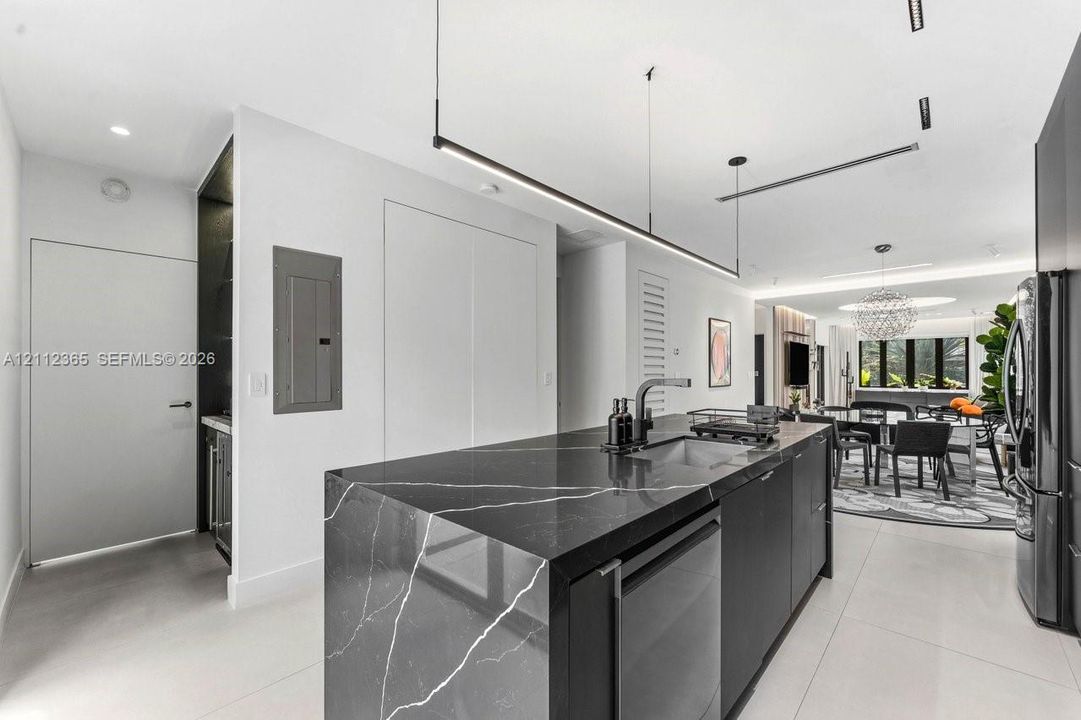 Kitchen island featuring dark veined stone surfacing, integrated cabinetry, undermount sink with a gooseneck faucet, and linear pendant lighting