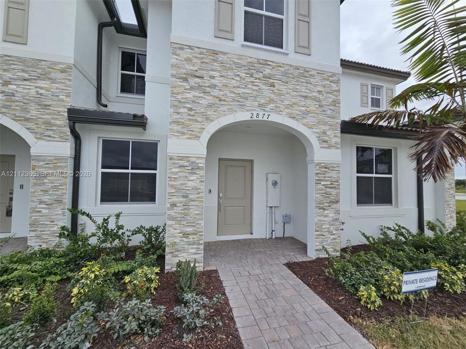 Stucco exterior featuring stacked stone accents, arched entryway, paved walkway, and multi-pane windows