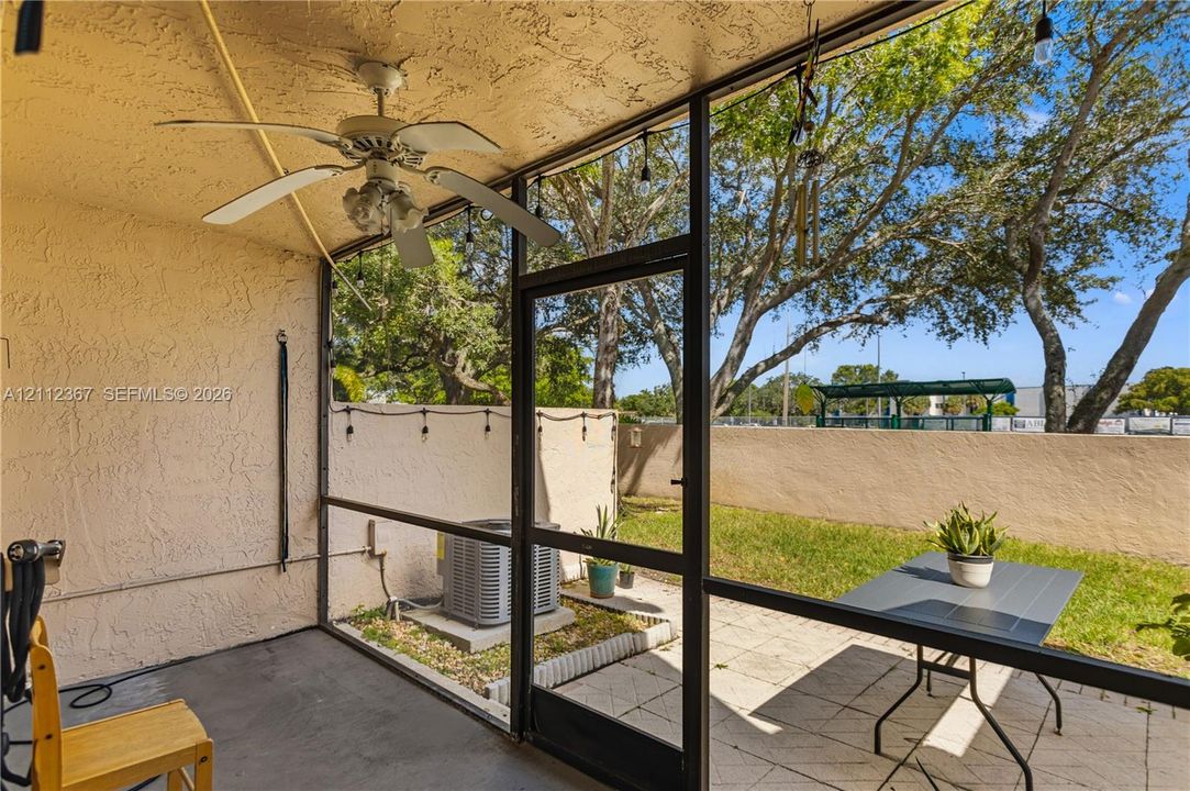 Screened-in patio featuring a textured ceiling, ceiling fan with light fixture, concrete flooring, and a paved outdoor area
