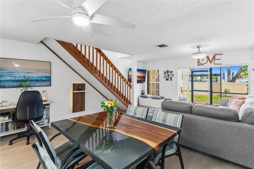 Open living area featuring wood-finish flooring, a staircase with wooden balusters, dual ceiling fans with integrated lighting, and glass sliding doors
