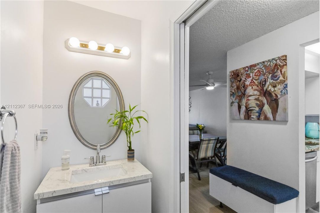Bathroom vanity featuring a stone-composite countertop, undermount sink, oval wall-mounted mirror, and a four-light fixture