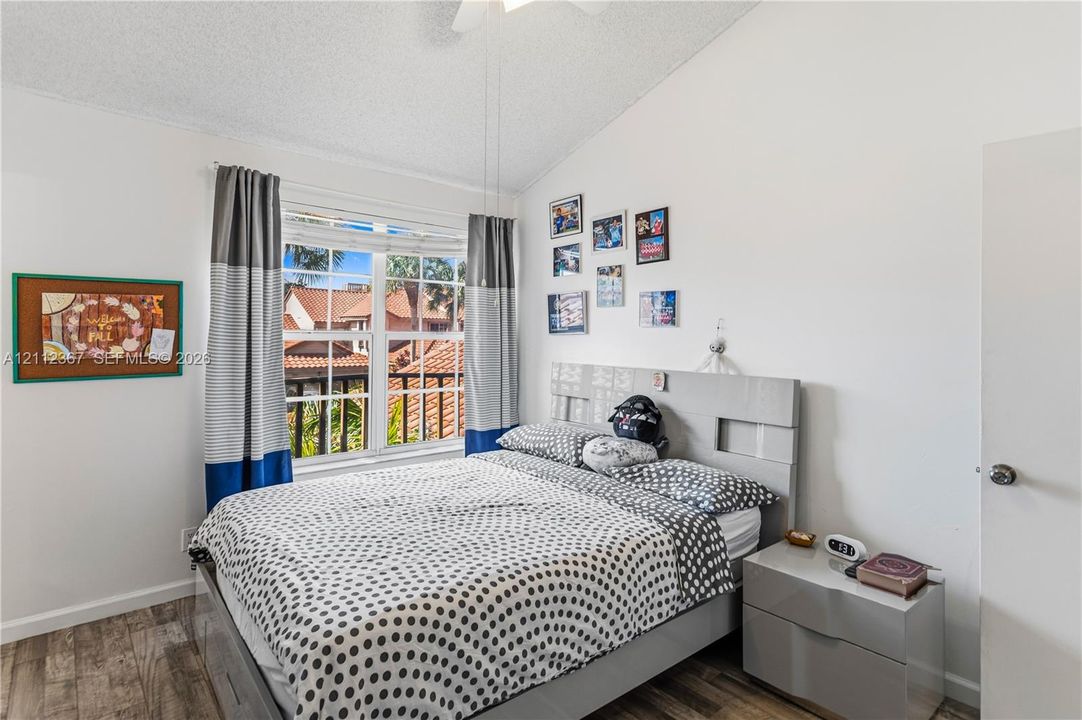 Vaulted ceiling, wood-finish flooring, multi-pane window, and white interior walls