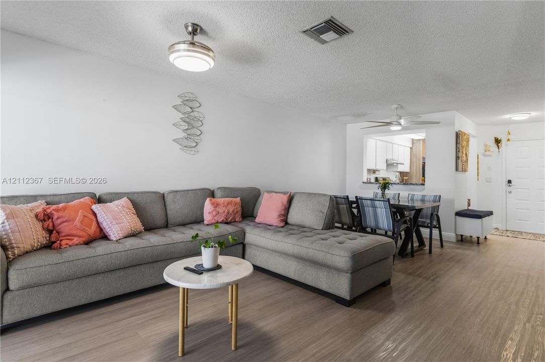 Living area featuring wood-finish flooring, ceiling-mounted light fixtures with integrated fans, and a pass-through window to the kitchen
