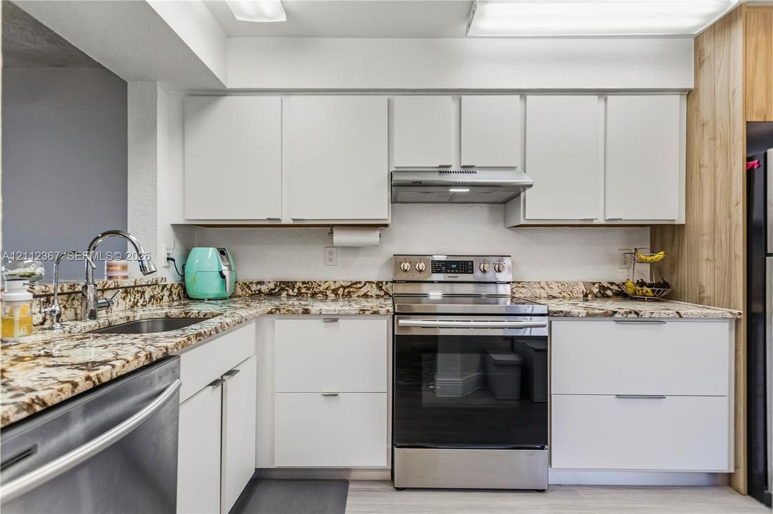 Kitchen featuring flat-panel white cabinetry, stone-surface countertops, stainless steel appliances, a pull-down kitchen faucet, and wood-finish wall paneling
