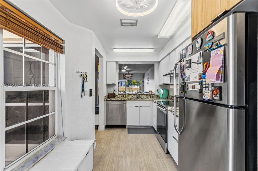 Kitchen featuring stainless steel appliances, white cabinetry, stone-surface countertops, and wood-finish flooring