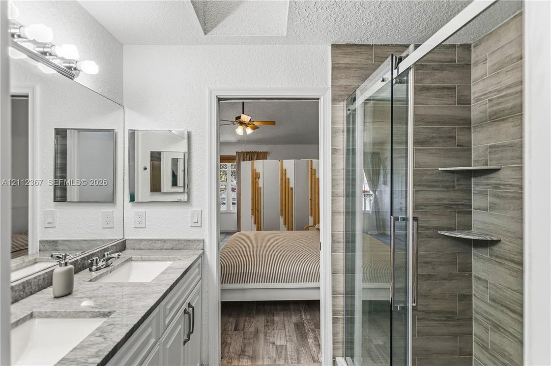 Dual-sink vanity with stone-finish countertop, full-width wall mirror, and walk-in shower with horizontal tile surround and integrated shelving