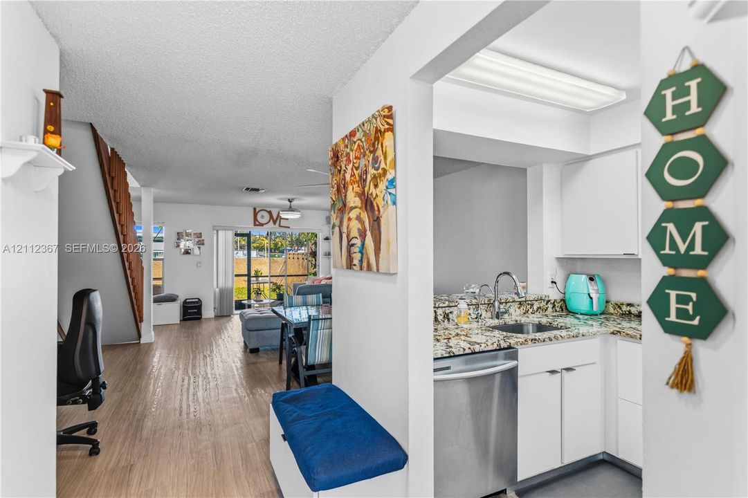 Kitchen featuring stone-finish countertops, stainless steel dishwasher, and white cabinetry, paired with wood-finish flooring and a staircase with an open-riser design