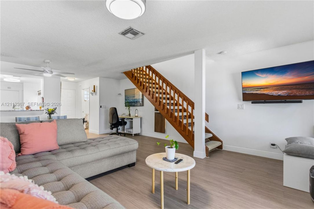 Open-concept interior featuring wood-finish flooring, a central wood staircase with open railings, flush-mount ceiling lighting, and a neutral color palette