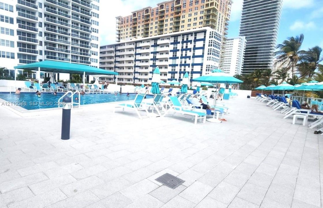 Swimming pool deck featuring light-colored stone pavers and a covered pavilion