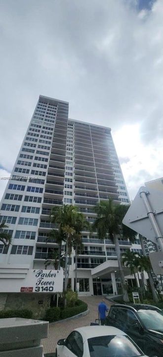 High-rise residential exterior featuring expansive private balconies, a covered porte-cochère entrance, and mature palm landscaping