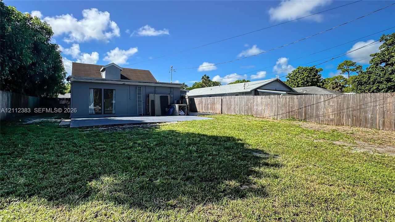 Expansive backyard featuring a grass lawn, privacy fencing, and a concrete patio