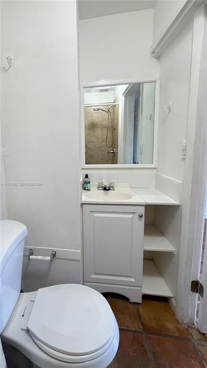 Bathroom featuring a vanity with integrated shelving, inset sink, framed wall mirror, and terra-cotta tile flooring