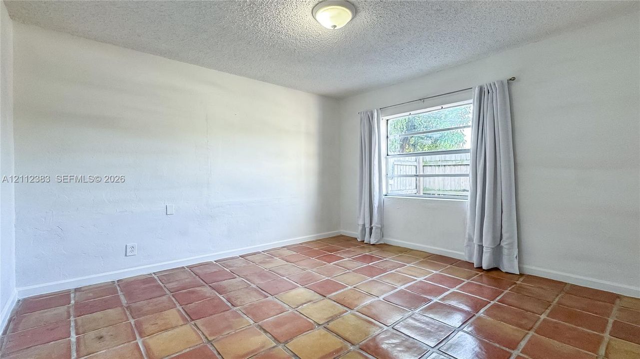 Interior space featuring terracotta-style tile flooring, textured ceiling, central flush-mount lighting, and a single-hung window
