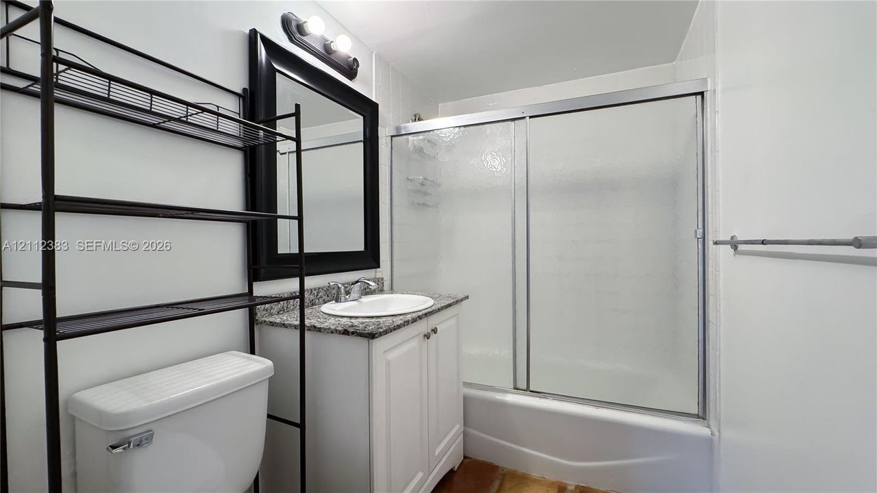 Bathroom featuring a white vanity with a stone-finish countertop, undermount sink, framed wall mirror, and a tub-shower combination with sliding glass doors