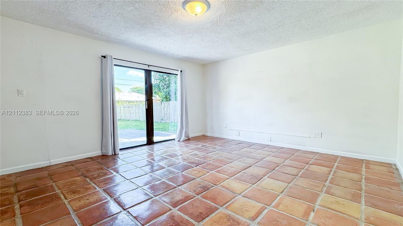 Interior room featuring terracotta tile flooring, sliding glass door, flush-mount lighting, and neutral wall paint