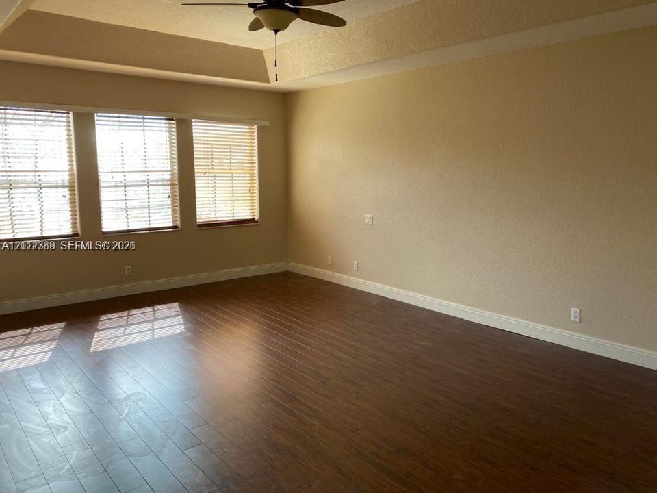 Interior space featuring wood-finish flooring, a tray ceiling, and a ceiling fan with integrated lighting