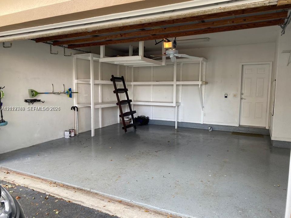 Garage featuring an epoxy-coated floor, integrated built-in shelving, overhead storage, and an exterior access door