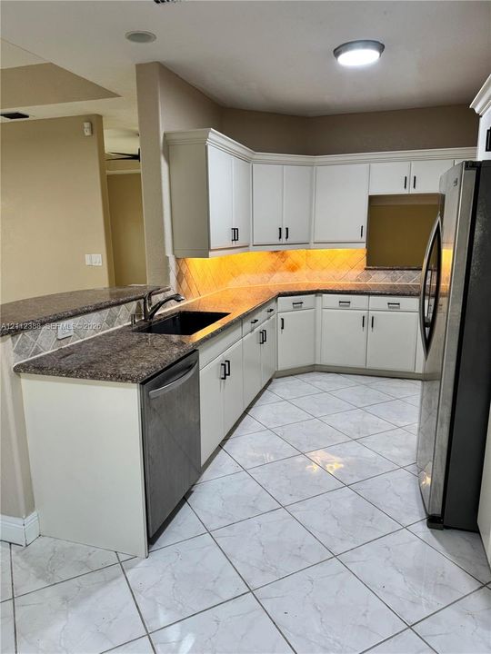 Kitchen featuring white cabinetry with matte black hardware, stone-finish countertops, tiled backsplash, and neutral-toned tile flooring