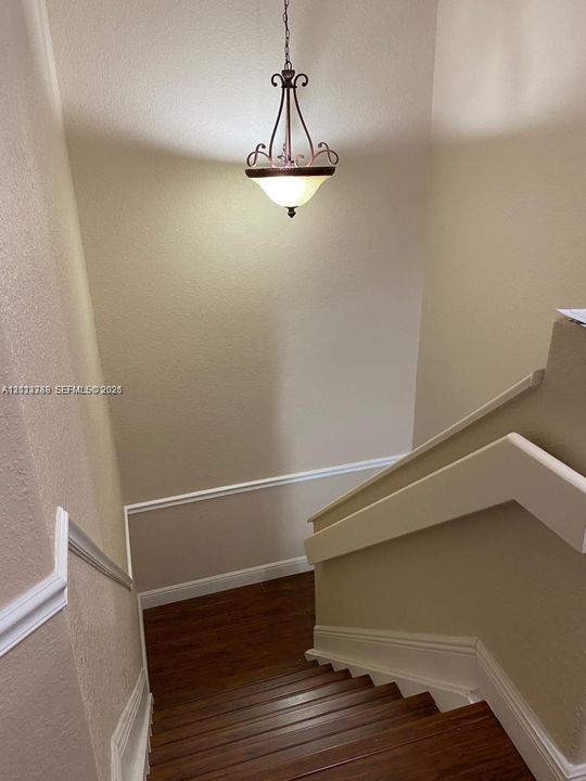 Staircase featuring wood-finish treads, a solid wall-mounted handrail, decorative chair rail molding, and a suspended metal chandelier with frosted glass