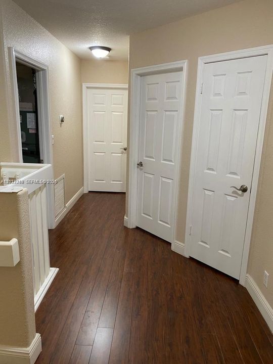Hallway featuring wood-finish flooring, six-panel interior doors, and a flush-mount ceiling light fixture