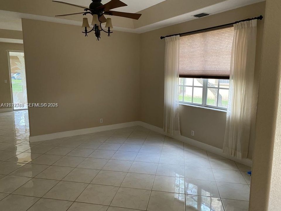 Room featuring large-format tile flooring, a tray ceiling, and a ceiling fan with integrated multi-light fixture