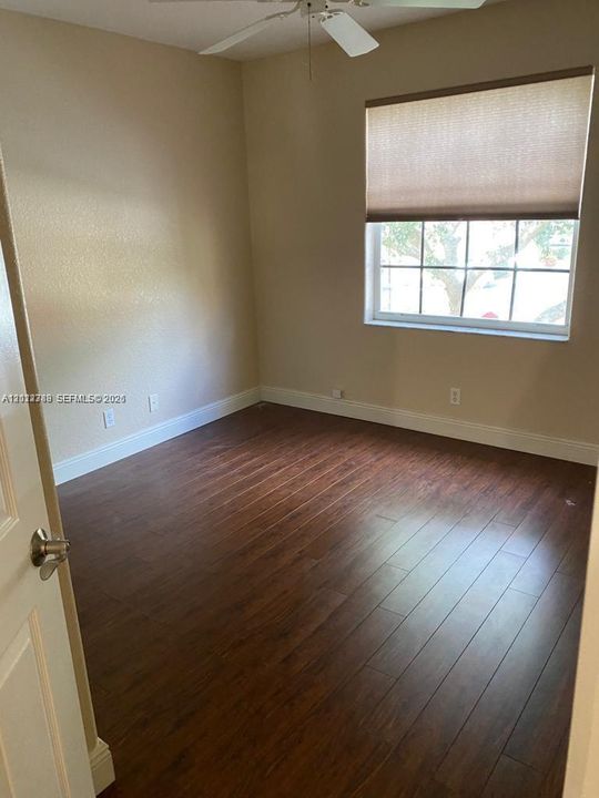 Room featuring dark wood-finish flooring, a multi-pane window with a neutral roller shade, and a ceiling fan