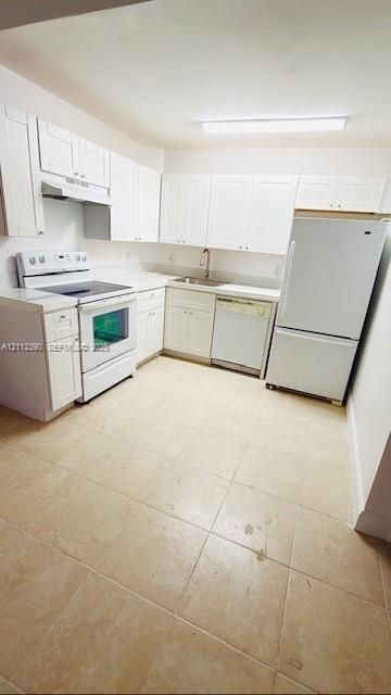 Kitchen featuring white cabinetry, solid-surface countertops, tile flooring, and integrated white appliances