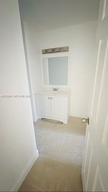 White vanity cabinet with a solid surface countertop, rectangular mirror, multi-bulb vanity light, and neutral tile flooring