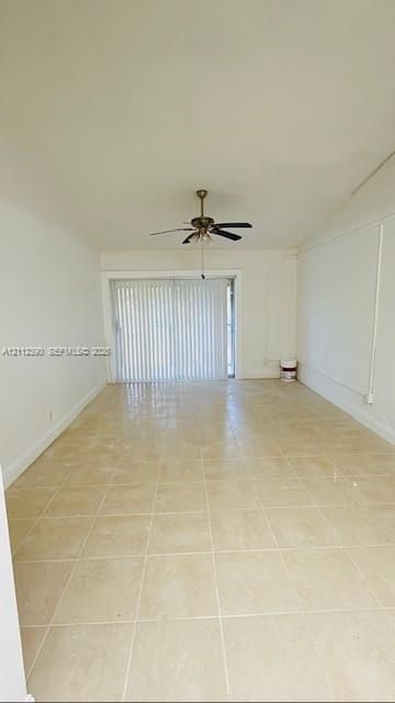 Interior space featuring large-format neutral floor tile, a vaulted ceiling, and a central ceiling fan with integrated lighting