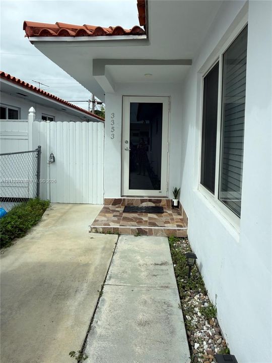 Exterior entry featuring a red tile roof, white stucco siding, multi-tonal stone-finish porch, and a glass-paneled front door